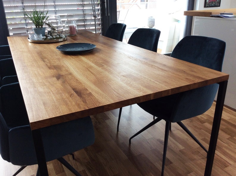 May include: A wooden dining table with a natural finish and black metal legs. The table is surrounded by six dark blue velvet chairs.