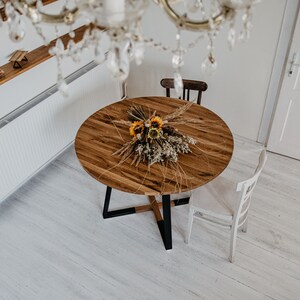 May include: A round wooden dining table with a black metal base. The table is set with a bouquet of dried flowers and grasses.