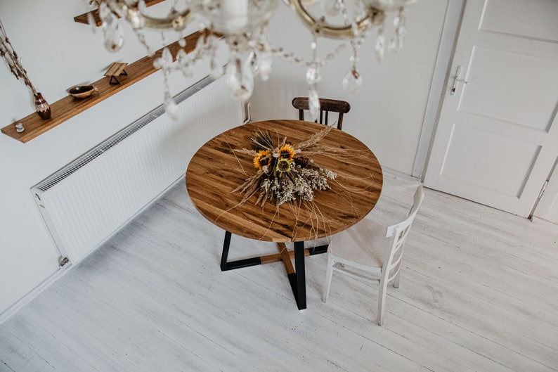 May include: A round wooden dining table with a black metal base. The table is set with a bouquet of dried flowers and grasses.