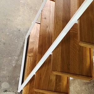 Puede incluir: Una estanter&iacute;a de metal blanco con cuatro estantes de madera. Los estantes son de madera natural con un acabado marr&oacute;n claro. Los estantes est&aacute;n inclinados y la unidad se ve desde arriba.
