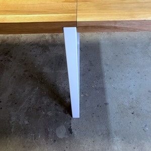 May include: A white table leg extends from a wooden table top, resting on a concrete floor.
