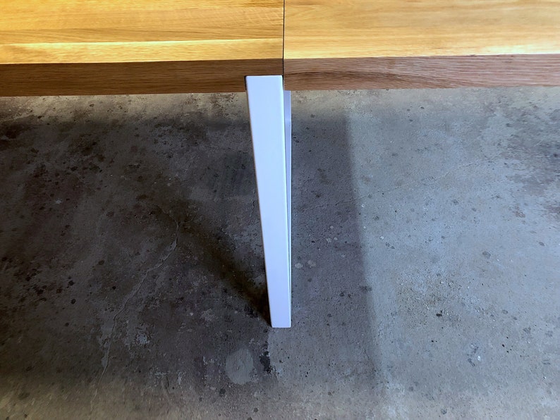 May include: A white table leg extends from a wooden table top, resting on a concrete floor.