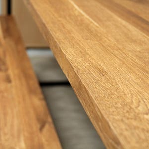 May include: Close-up of a wooden table with a natural wood grain finish. The table has a light brown color and appears to be made of solid wood. The image highlights the texture and detail of the wood.