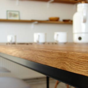May include: A close-up of a wooden countertop with a natural wood grain. The countertop has a black metal edge. White mugs and a white electric kettle are on the countertop. Shelves are in the background.
