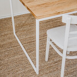 May include: A wooden table with a white metal frame and a white chair. The table has a light brown wooden top. The chair has a curved back and seat. The table and chair are on a woven brown rug.