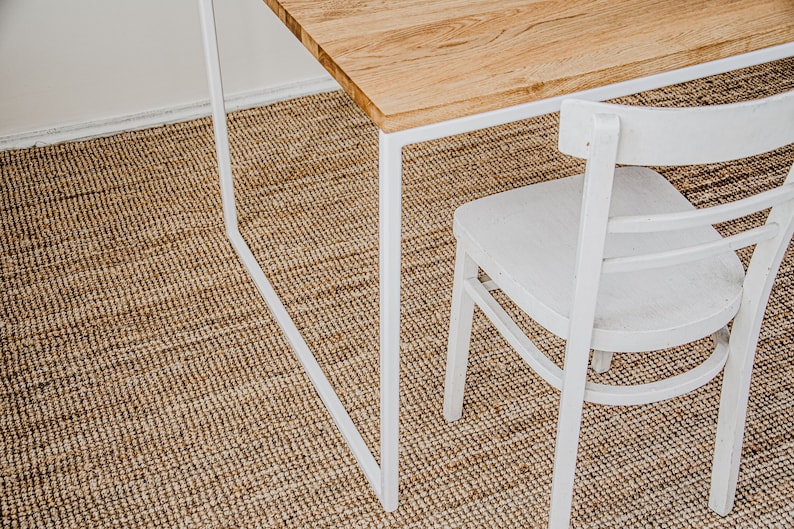 May include: A wooden table with a white metal frame and a white chair. The table has a light brown wooden top. The chair has a curved back and seat. The table and chair are on a woven brown rug.