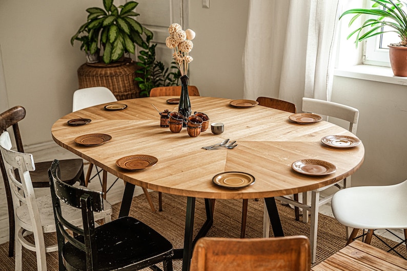 May include: A round wooden dining table with black metal legs, set with plates and cutlery. The table is surrounded by chairs, including a black chair with a woven seat and a white chair with a woven seat.
