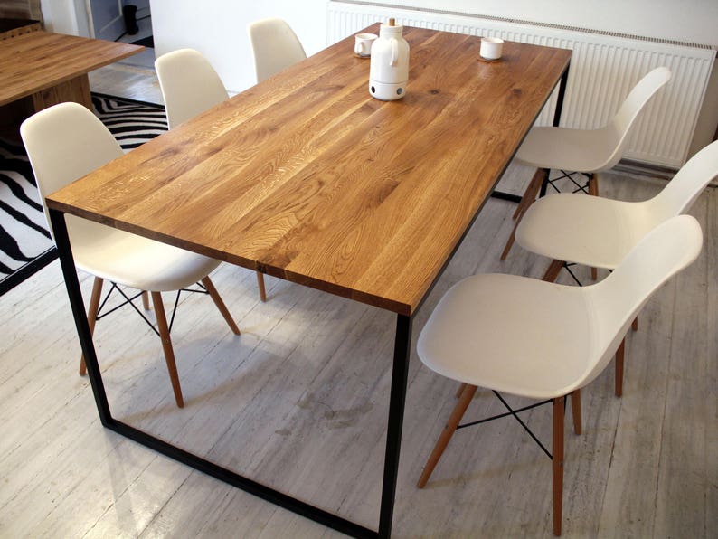 May include: A rectangular wooden dining table with a black metal frame. The table is surrounded by six white chairs with wooden legs. The table has a natural wood finish and is made of solid wood.