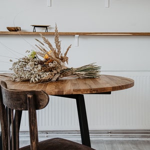 May include: A round wooden table with a black metal base and a single wooden chair. A bouquet of dried flowers sits on the table.