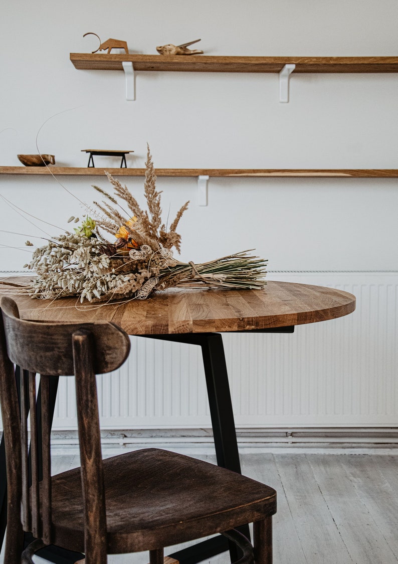 May include: A round wooden table with a black metal base and a single wooden chair. A bouquet of dried flowers sits on the table.