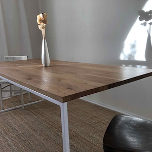 May include: A white metal dining table with a wood top. The table is set with a vase of dried flowers.