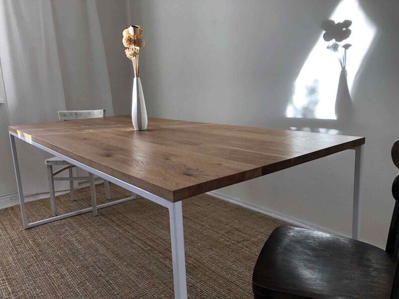 May include: A white metal dining table with a wood top. The table is set with a vase of dried flowers.