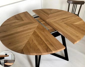 Könnte beinhalten: Ein runder Esstisch aus Holz mit einem schwarzen Metallgestell. Die Tischplatte ist aus Eichenholz und hat ein Chevron-Muster. Der Tisch ist ausziehbar, mit einer Platte, die hinzugefügt werden kann, um die Größe des Tisches zu vergrößern.