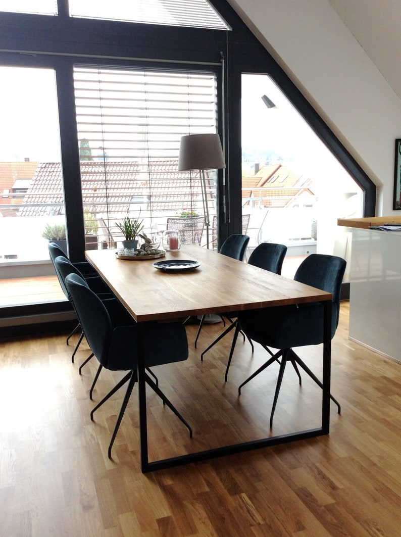 May include: A wooden dining table with a black metal frame and six dark blue velvet chairs. The table is set with a plate, a candle, and a plant.