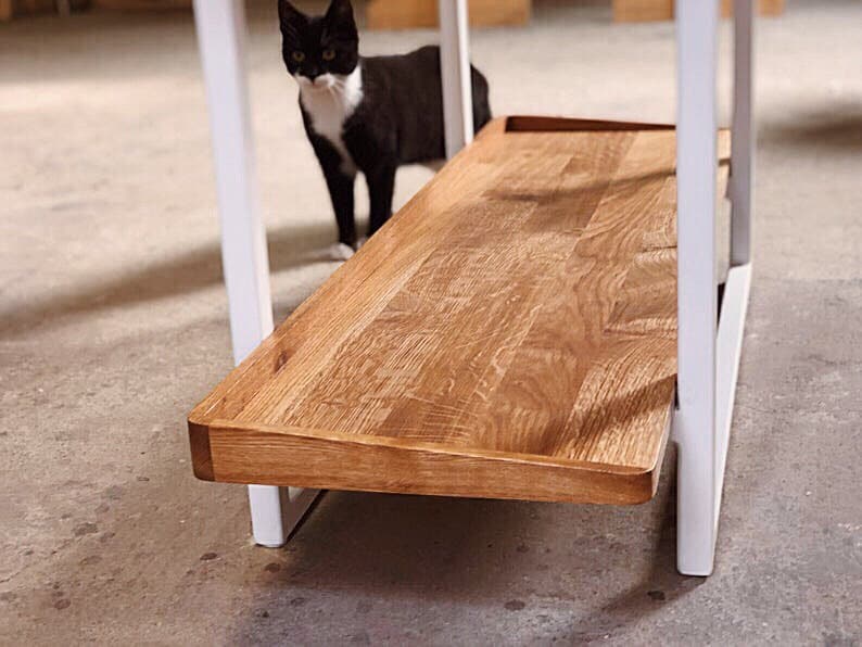 Puede incluir: Un marco de mesa de metal blanco con un estante de madera. El estante est&aacute; hecho de madera natural con un acabado marr&oacute;n claro. La mesa est&aacute; en una habitaci&oacute;n con un suelo blanco.