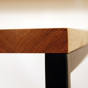May include: Close-up of a wooden table top with a black metal frame. The wood grain is visible and the table top is smooth.