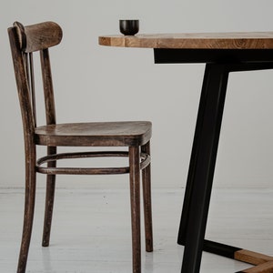 May include: A dark brown wooden chair with a curved back and a round table with a black metal base. The table top is made of light brown wood.