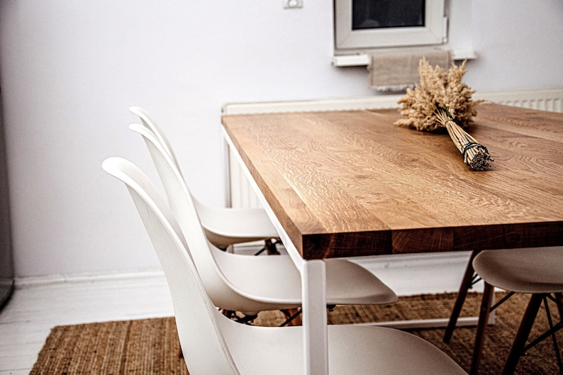 May include: A wooden dining table with a white metal frame and four white chairs. The table has a natural wood finish and is decorated with a bouquet of dried wheat.
