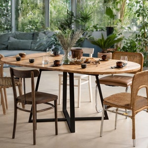 K&ouml;nnte beinhalten: Ein ovaler Esstisch aus Holz mit einem schwarzen Metallgestell, umgeben von sechs St&uuml;hlen. Der Tisch ist mit Geschirr, Tassen und einer Blumenvase gedeckt. Die St&uuml;hle sind in verschiedenen Stilen gehalten, darunter Korbgeflecht und Holz.