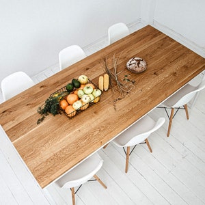 May include: A wooden dining table with a white frame and six white chairs. The table is set with a basket of fruit, a loaf of bread, and some corn on the cob.