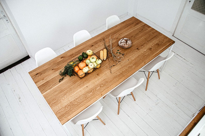 May include: A wooden dining table with a white frame and six white chairs. The table is set with a basket of fruit, a loaf of bread, and some corn on the cob.