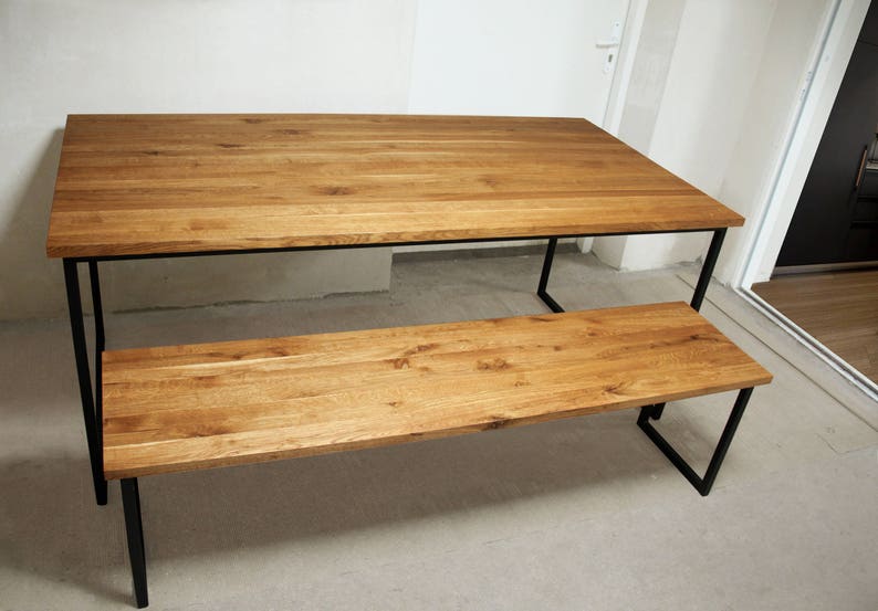 May include: A rectangular wooden dining table and matching bench. The tabletop and bench seat are made of light brown wood. The table and bench have black metal legs. The table is approximately 72 inches long.
