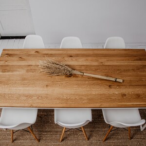 May include: A long wooden dining table with a white metal frame and six white chairs. A dried flower arrangement is placed in the center of the table.