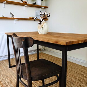 May include: A wooden dining table with a black metal frame and a single wooden chair. The table is set with a white ceramic vase filled with cotton flowers.
