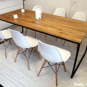 May include: A rectangular wooden dining table with a black metal frame. The table is surrounded by six white chairs with wooden legs. The table is large enough to seat 4-12 people.