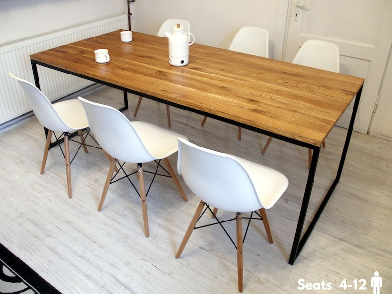 May include: A rectangular wooden dining table with a black metal frame. The table is surrounded by six white chairs with wooden legs. The table is large enough to seat 4-12 people.