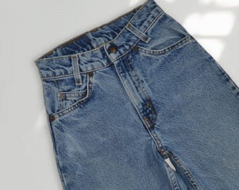 May include: High-waisted blue denim jeans featuring a classic five-pocket design, a metal button closure, a zippered fly, and belt loops. The fabric displays a medium wash with visible stitching details along the waistband and pockets.