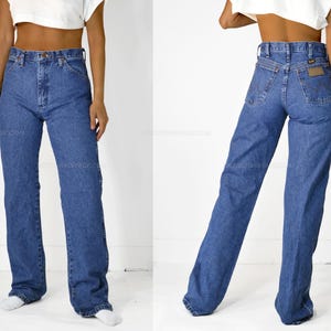 May include: A pair of blue denim jeans with a high waist and a straight leg fit. The jeans have a classic five-pocket design and a leather patch on the back waistband.