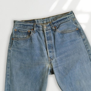 May include: Light blue denim jeans with a button fly, classic five-pocket design, and copper rivets. The jeans have a faded wash and a straight leg fit. A timeless wardrobe staple.