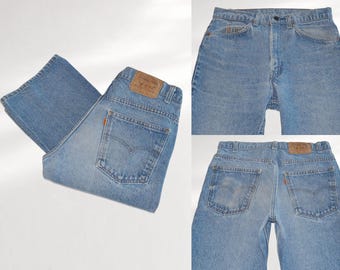 Może przedstawiać: Jasnoniebieskie jeansy z denimu z brązową skórzaną naszywką na tylnym pasku, pomarańczową metką na tylnej kieszeni, zapięciem na guziki, szlufkami na pasek i klasycznym krojem z pięcioma kieszeniami oraz widocznymi przeszyciami na całości.