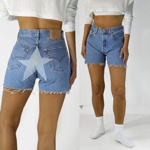 May include: Light blue denim shorts with a raw hem. The shorts feature a large, light-colored star design on the back. The shorts are a classic style, perfect for casual wear.