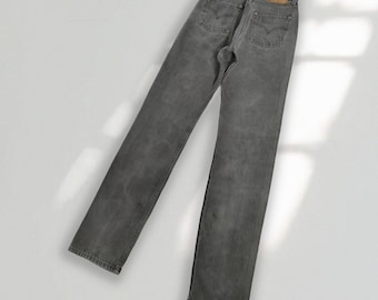 May include: A pair of high-waisted gray denim jeans featuring a straight-leg cut, two back pockets with stitched arcuate detailing, a tan leather-like patch on the waistband, and a small red fabric tab attached to the right rear pocket seam.