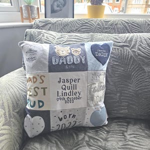May include: A square patchwork memory cushion made from assorted grey, blue and white fabric squares. The cushion features embroidered text including "Daddy & me", "Jasper Quill Lindley 09th October 2022", "born in 2022" and "I love my DADDY", alongside heart and bear motifs.