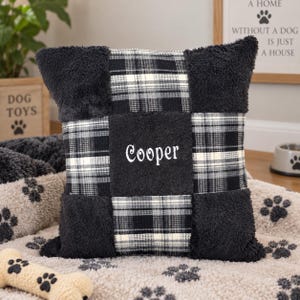 May include: A square throw pillow featuring a patchwork design of black fuzzy fabric and a black, white, and grey plaid pattern. The centre black fuzzy square is embroidered with the name Cooper in white script lettering.