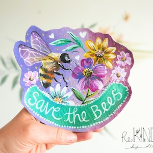 Peut inclure: Une œuvre d'art peinte à la main représentant une abeille rayée orange et noire, entourée de fleurs roses, jaunes et violettes. Le texte "Save the Bees" est écrit en blanc sur une bannière verte.