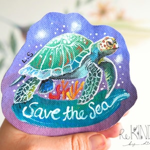 Op de afbeelding: Een handgeschilderde patch met een zeeschildpad met een groen en blauw schild, zwemmend boven koraal. De patch heeft een paarse achtergrond met witte stippen en de woorden "Save the Sea" in witte letters. De patch heeft een onregelmatige vorm.