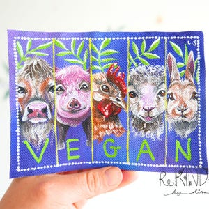 May include: A blue rectangular painting featuring the faces of a cow, pig, chicken, sheep, and rabbit. The word "VEGAN" is written in green. Green leaves and vertical lines separate the animals.