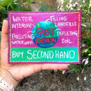 Op de afbeelding: Een rechthoekige patch met een roze achtergrond, een centrale wereldbolafbeelding en de tekst "FAST FASHION" in rood en blauw. De omringende tekst bevat "WATER INTENSIVE," "FILLING LANDFILLS," "POLLUTING WATER WAYS" en "DEPLETING SOIL." Een groene banner leest "BUY SECOND HAND."