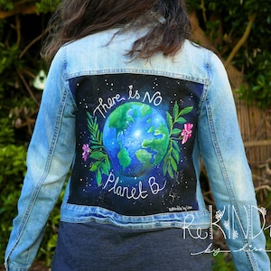 Könnte beinhalten: Hellblaue Jeansjacke mit einem bemalten Design auf dem Rücken. Das Design zeigt eine blaue und grüne Erde, umgeben von Blättern und rosa Blumen, mit dem Text "There is No Planet B."