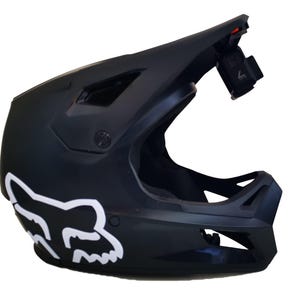 May include: Black full-face motorcycle helmet with a white Fox logo on the side. The helmet has a built-in visor and a mount for a camera on the top.