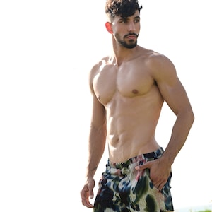 May include: Shorts with a colorful abstract pattern in shades of blue, green, and red. The shorts have a drawstring waist and pockets. The model is standing outside in the sun.