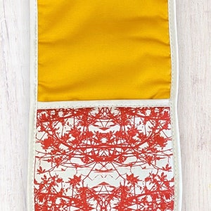 May include: A white oven mitt with a red floral pattern and a yellow lining. The mitt is designed to protect hands from heat while cooking or baking.