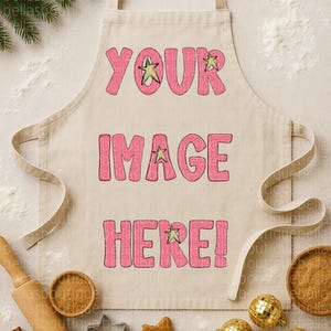 Peut inclure: Un tablier beige avec le texte "YOUR IMAGE HERE!" en rose, orné d'étoiles. L'image comprend des fournitures de pâtisserie comme des bâtons de cannelle, des emporte-pièces en forme d'étoile et des ornements dorés en forme de boule disco.