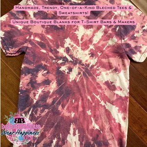 May include: A short-sleeved t-shirt with a tie-dye pattern in shades of burgundy, white, and purple. The shirt features text that reads "HANDMADE, TRENDY, ONE-OF-A-KIND BLECHED TEES & SWEATSHIRTS!" and "UNIQUE BOUTIQUE BLANKS FOR T-SHIRT BARS & MAKERS".