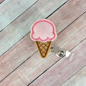 Könnte beinhalten: Rosa und brauner Filz-Eiswaffel-Badge-Rollenhalter mit einem durchsichtigen, einziehbaren Badge-Halter aus Kunststoff.