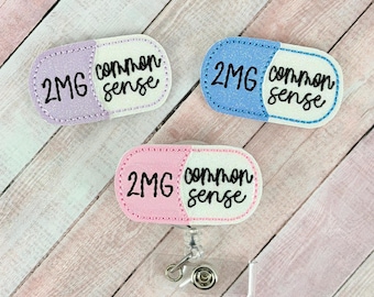 May include: Three badge reels in the shape of a pill, each with a different color scheme. The left side of each pill is either lavender, blue, or pink, and the right side is white. Each badge reel has the text "2MG common sense".